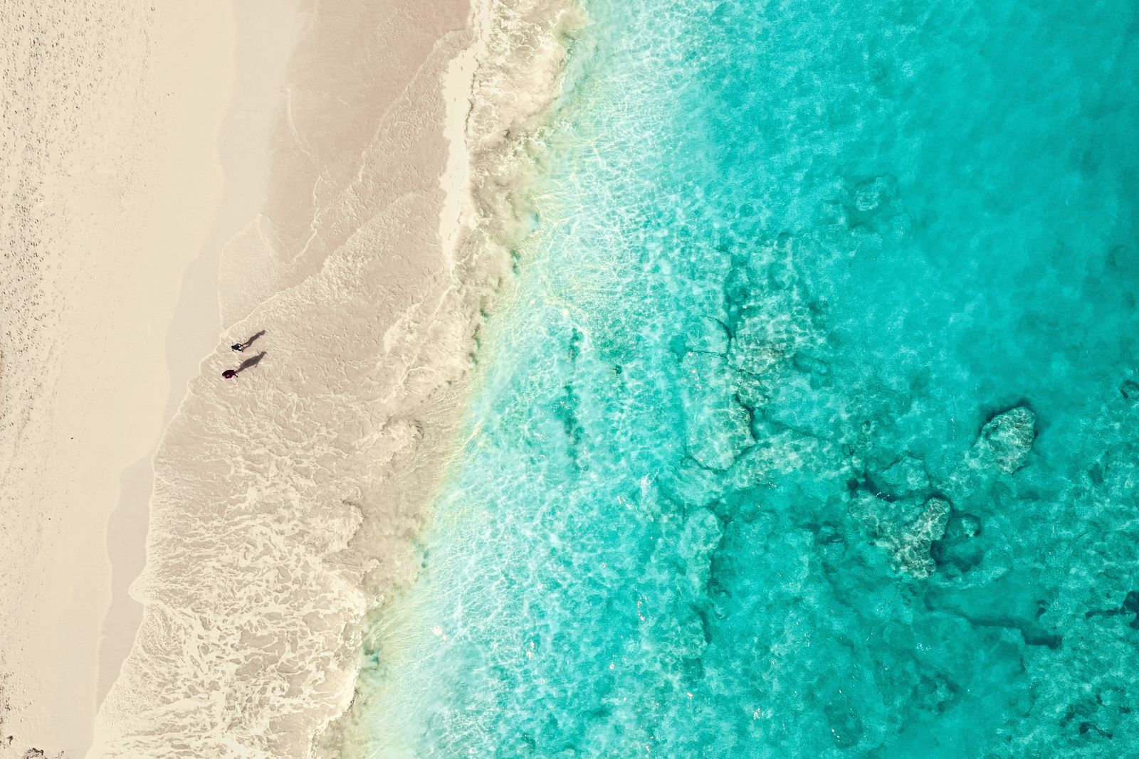 Two people walking along wet sand at the shoreline, seen from above