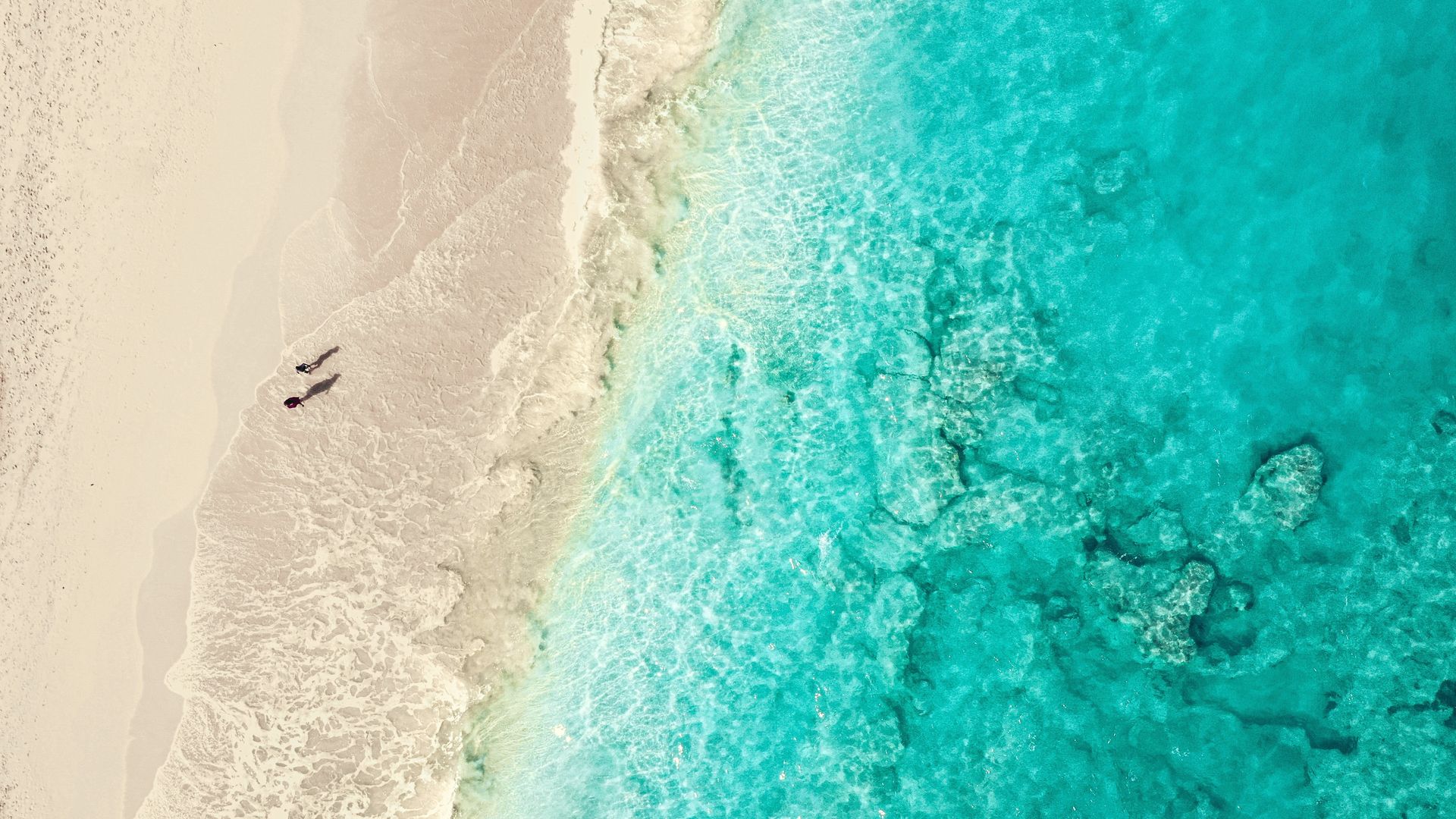 Aerial view of soft turquoise water meeting pale sand on the shoreline