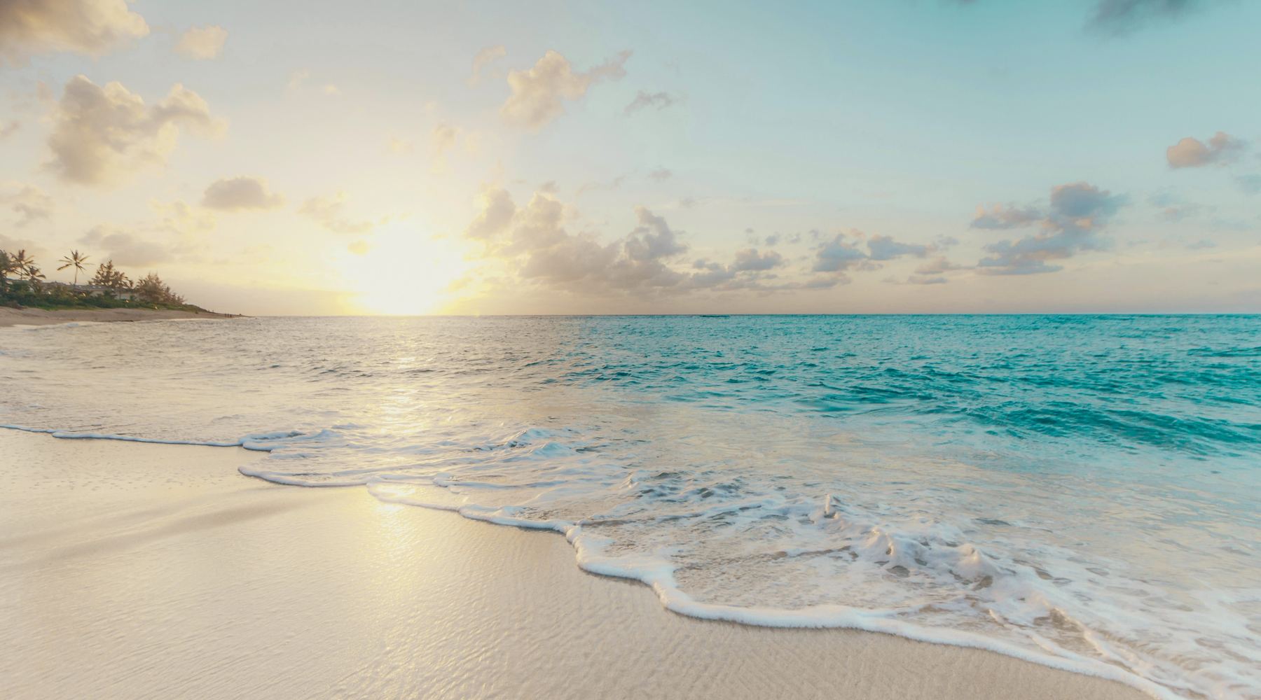 Sunrise over a calm beach, the tide washing up pale sand