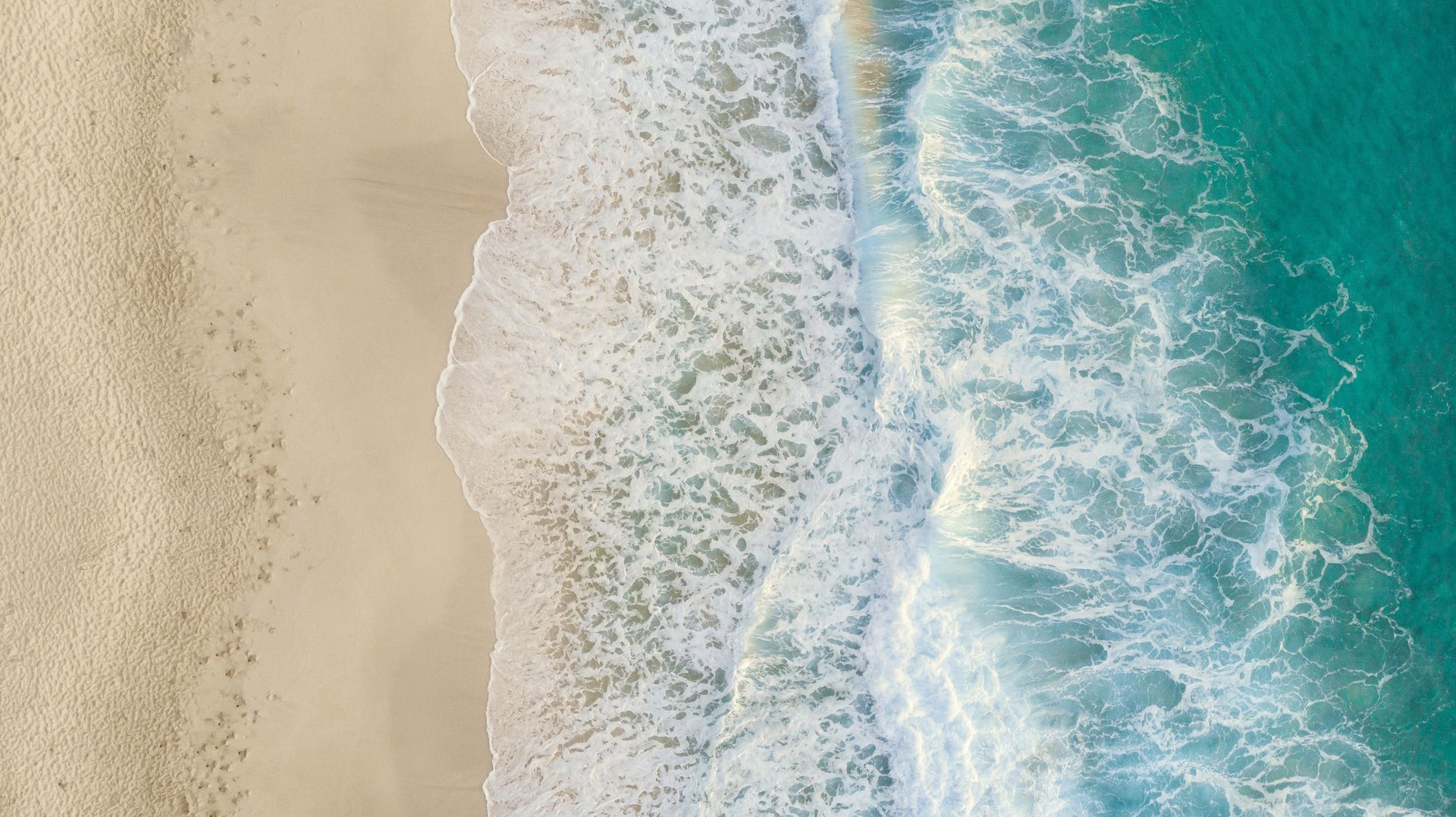 Aerial view of white foam breaking over vivid turquoise water