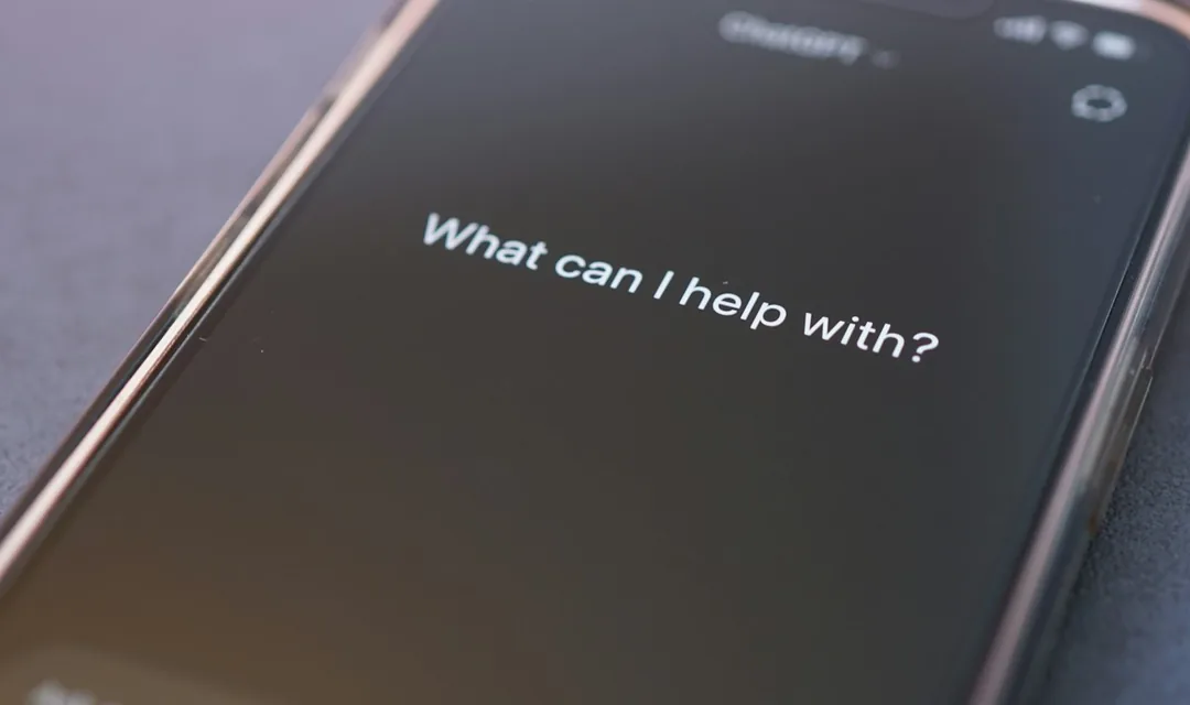 A phone on a desk showing an AI assistant asking what can I help with