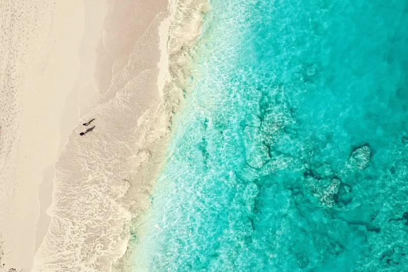 Two people walking along wet sand at the shoreline, seen from above