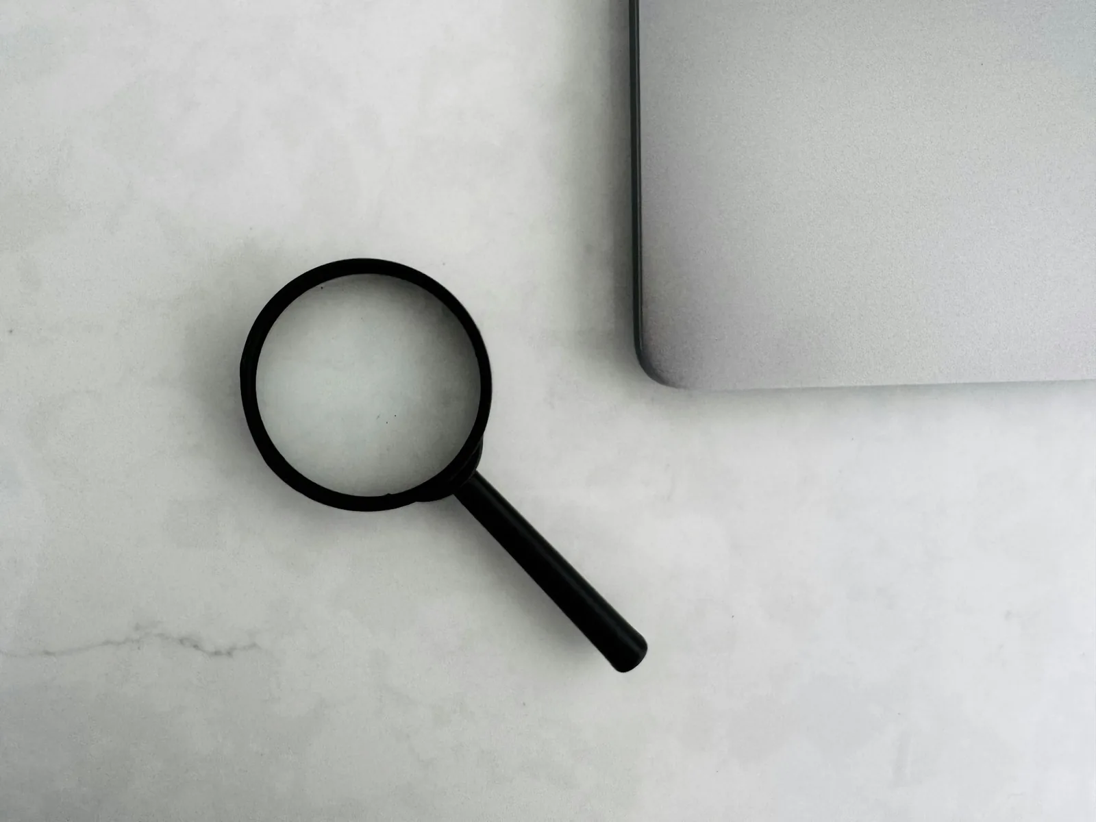 A magnifying glass resting beside a laptop on a pale marble desk