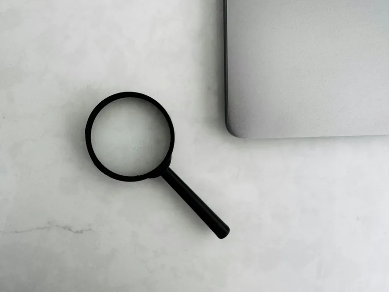 A magnifying glass resting beside a laptop on a pale marble desk