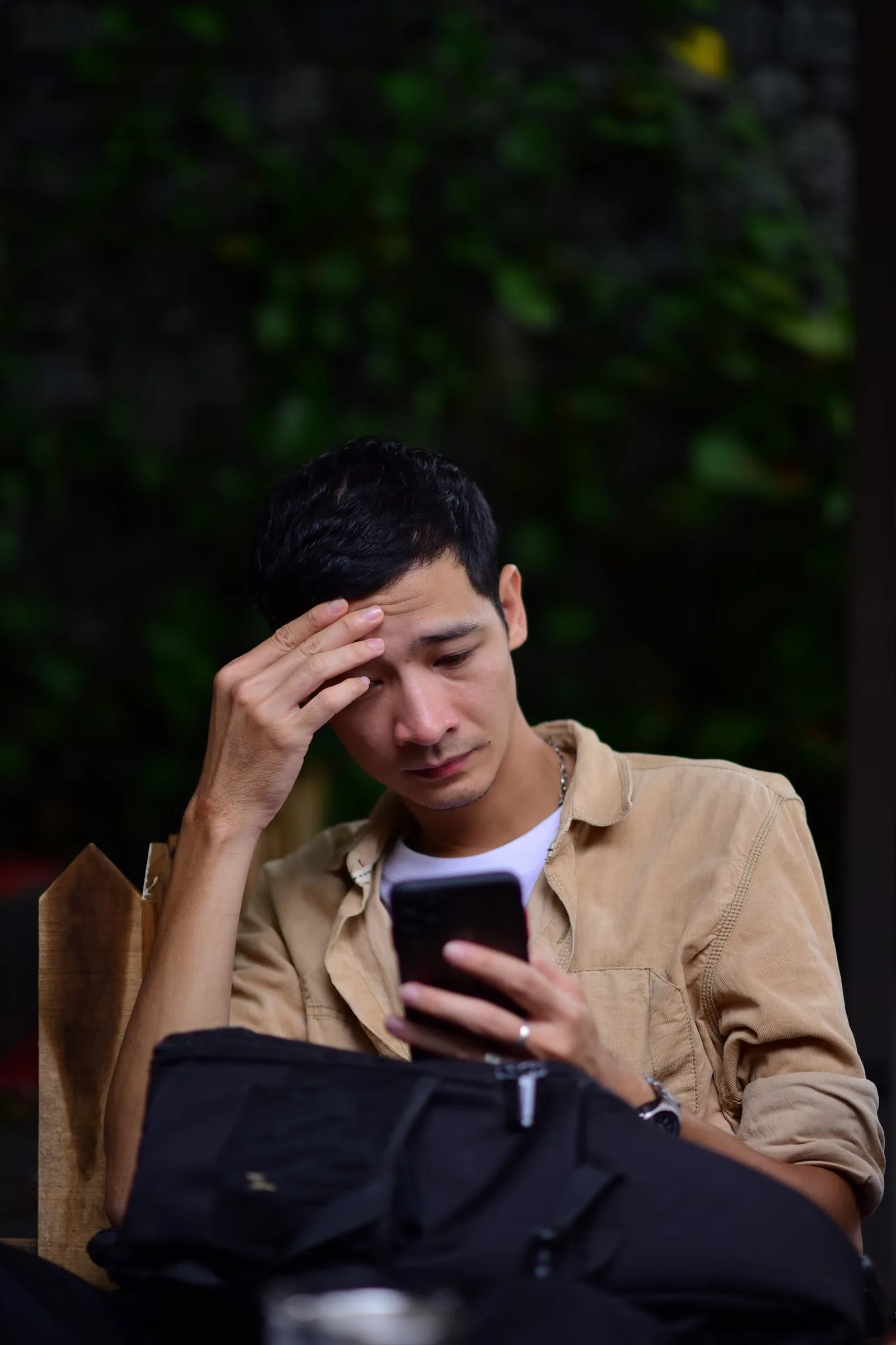 Small business owner outdoors reading a bad review on his phone, hand to his forehead