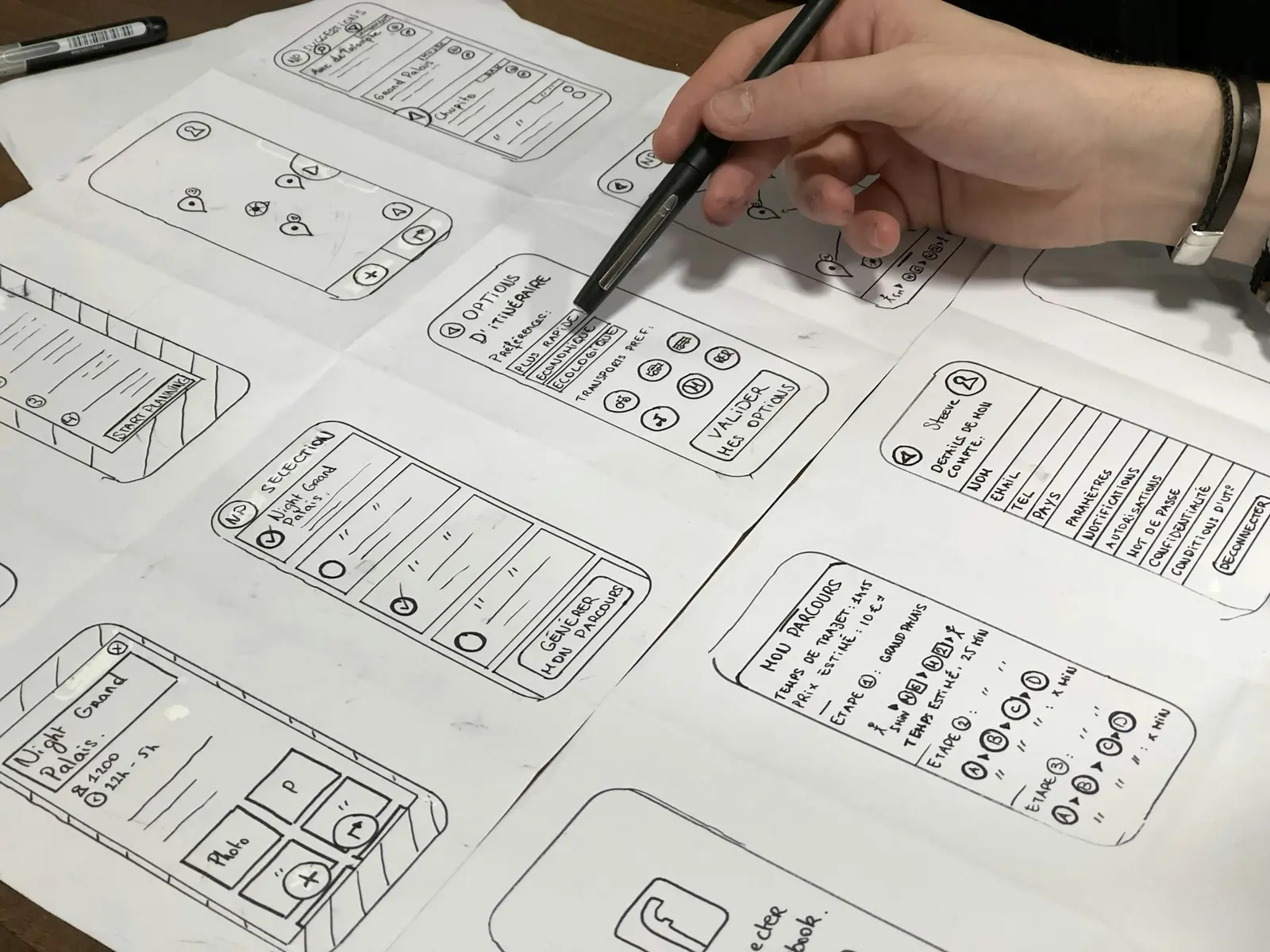 A hand sketching website wireframe layouts in pen across sheets of paper