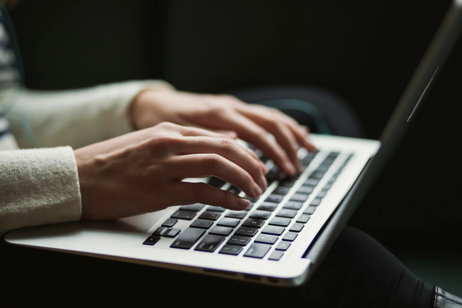 Hands typing an email on a silver laptop in a dimly lit room